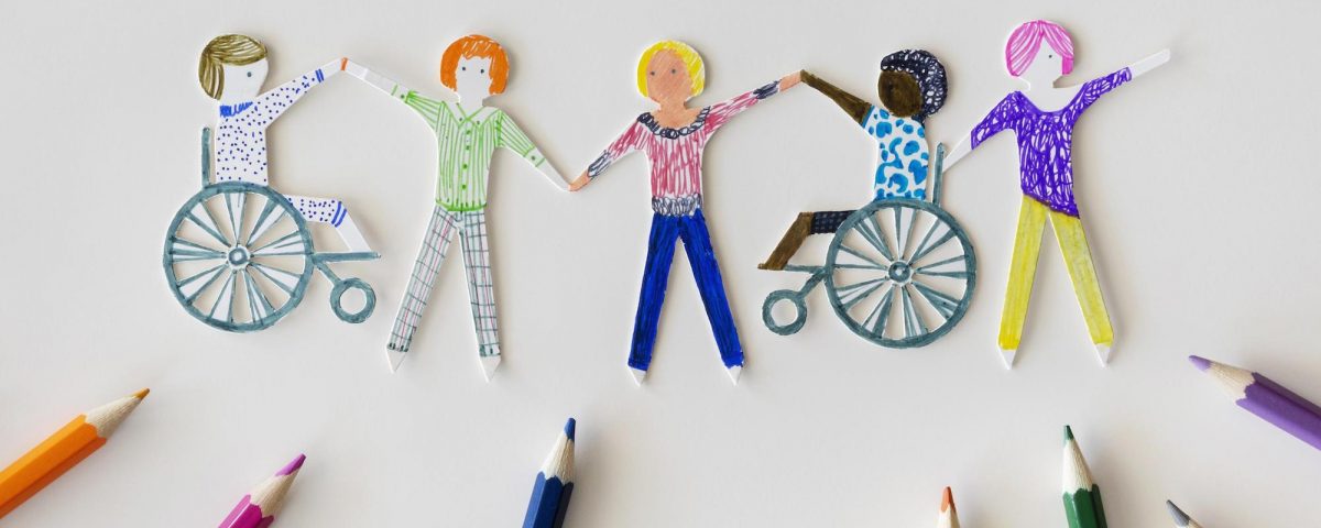 [Para cego ver] Imagem traz desenho multicolorido de pessoas de mãos dadas numa folha de papel. Duas dessas pessoas são cadeirantes. Há vários lápis de cor sobre o papel.