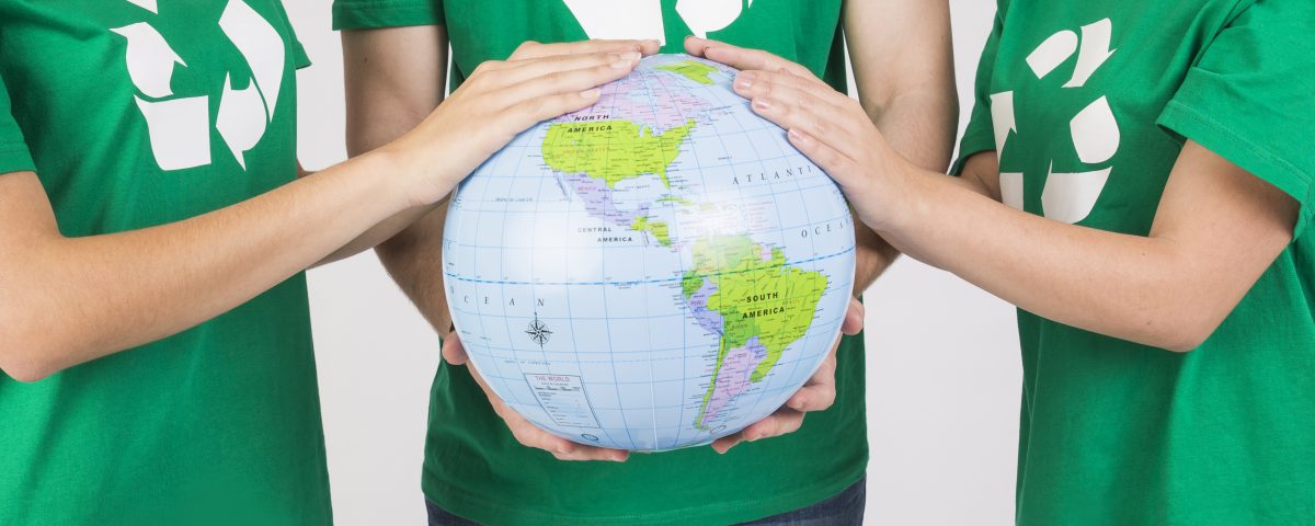 [Pra cego ver] Pessoas com camisetas verdes e com símbolo da reciclagem em destaque seguram o globo